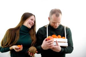 Mann und Frau Früchte Äpfel Mandarinen Persimmon Kokosnuss jung Mädchen lächelnd lacht Mann stellen Korb um Hals sieht aus in es Weiß Hintergrund Konzept gesund Ernährung Vitamine Leistungen gut Stimmung Spaß foto