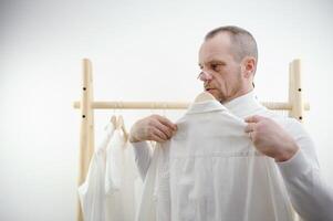 Mann isoliert im Vorderseite von Weiß Hintergrund halten zwei Hemden das Mann kippen entscheiden welche Hemd zu tragen. nicht Sein fähig zu entscheiden auf das Wahl von Kleidung. foto