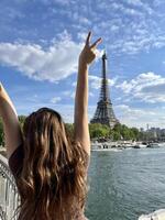 ein heiter Teen Mädchen steht gegen das Hintergrund von das Eiffel Turm im ein schön Kleid, sie angehoben ihr Hand, Sie können werben ein Reise Agentur Ausflug zu Paris Frankreich foto