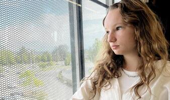 europäisch Mädchen mit blond lange Haar im ein Weiß Hemd Fahrten im ein Skytrain sie traurig sieht aus aus das Fenster sie ist traurig warten zum ihr ein lange Straße draußen das Fenster blitzt Natur Häuser Vancouver surrey foto