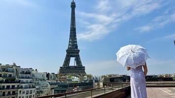 ein schön jung Mädchen im ein Sommer- Kleid steht gegen das Hintergrund von das Eiffel Turm mit ein Spitze Regenschirm, sie angehoben ihr Hand und wie wenn nehmen aus Dort ist ein Platz zum Werbung Reise Agentur foto