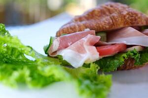 Croissant Sandwich mit Fleisch Jamon Prosciutto mit Tomate Grüner Salat Essen Reich Stücke von Käse im Frühstück Frankreich auf ein Weiß Teller teuer Restaurant Hotel bekommen ein Stück von Fleisch mit ein Gabel foto