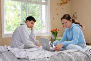 Jugendliche Bruder und Schwester Studie online beim Schule sitzen im das gleich Zimmer zusammen in der Nähe von Laptop online Konferenz aussehen zum Antworten auf das Internet jedermann hat ihr besitzen Gadget foto