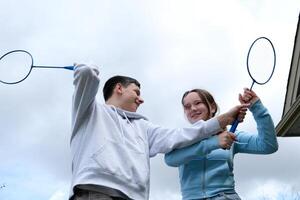 Kampf mit Badminton Schläger Jungs Mädchen schwingen jeder andere mit Schläger abspielen haben Spaß zuerst Liebe Teenager Beziehung wütend Sein zufrieden Lächeln Emotionen Übergang Alter jung Männer und Frauen foto