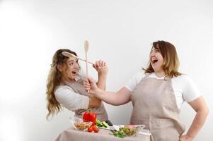 Küche Menschen Kampf 2 heiter Frauen Kampf gesund Essen Mama und Tochter Freundinnen Schürzen Küche Gemüse auf das Tabelle Glaswaren komisch Foto öffnen Kuchen Lachen machen Gesichter haben Spaß