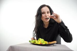 auf Weiß Hintergrund Frau im schwarz Kleider isst ein Salat und Fleisch mit ein Gabel sieht aus in das Rahmen Raum zum Text richtig Ernährung Weiß Hintergrund einer Frau geschmacklos Essen gezwungen Diät foto