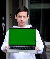 Grün Bildschirm Laptop ist ein Nahansicht Teen Junge im grau Kapuzenpullover halten Laptop mit Grün Bildschirm Produkt Anzeige Stern Schulter in der Nähe von seine Zuhause Lieferung köstlich Essen Raum zum Text kostenlos Raum Fotografie foto