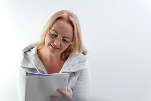 europäisch Frau mit Brille beißt Stift schreibt auf Blatt von Papier dokumentieren kommt oben mit Geschichte Schriftsteller Zeitschrift Design meditieren aussehen zu Seite denken blond Haar im Studio Weiß Hintergrund Autor von ein Buch foto