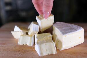 Komposition von Italienisch Käse, auf ein hölzern Schneiden Tafel. einer Hand nimmt das Messer und geht kaputt ein Paar von Stücke zu genießen das Qualität. foto