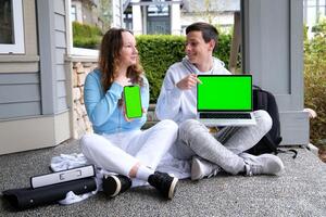 Grün Bildschirm Chromakey auf ein Laptop und auf das Telefon ein Kerl mit ein Mädchen Jugendliche sitzen auf das Veranda Licht Kleider kommunizieren halt ein Platz zum Ihre Werbung leeren Raum foto
