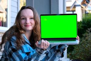 Teenager Mädchen im Hände mit Laptop Grün Bildschirm Chroma Schlüssel Werbung Teen sitzen auf Veranda beim Zuhause süß Gesicht zärtlich Lächeln Anzeige aussehen Hier wählen diese schön Produkt zufrieden glücklich gut sieht aus echt Menschen foto