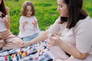 ein Frau und zwei Kinder sind Sitzung auf ein Decke im ein grasig Feld foto