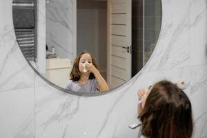 ein jung Mädchen weht Rotz von ihr Nase im Vorderseite von ein Spiegel foto