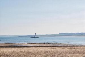 heiter Strand mit entfernt Leuchtturm im neubiggin-by-the-sea Strand foto