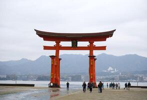 Miyajima Insel, Japan - - Dezember 5, 2023 - - Touristen gehen um das berühmt schwebend torii Tor von das itsukushima Schrein auf Miyajima Insel beim niedrig Tide foto