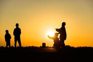 Kindersilhouette, die mit vielen Freunden Spaß macht und gegen den Sonnenuntergang spielt foto