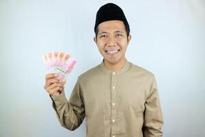 glücklich Ausdruck von asiatisch Muslim Mann halten Geld Rupiah Banknoten isoliert auf Weiß Hintergrund foto