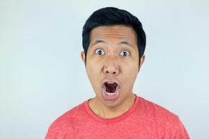 komisch Ausdruck von schockiert und überrascht asiatisch Mann tragen ein rot T-Shirt suchen beim das Kamera foto