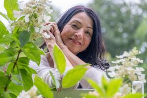 ein lächelnd midage Frau im ein Grün Blume Garten ist ausdrücken Glück und Freude von Lebensmitte hormonell Änderungen und kämpft. foto