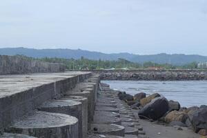 ein Mauer auf das Kante von das Strand und Meer mit ein einzigartig Oval gestalten Das Besucher können verwenden zu sitzen und genießen das Meer Aussicht Schuss auf hell Tag foto