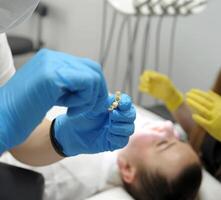 Nahansicht von Krankenschwester Hände verschmieren kleben Besondere Befestigung Material auf Patienten vorübergehend Zähne Prothetik Dental Behandlung im Hintergrund Gelb Handschuhe von Arzt Frau Gesicht im ein Dental Büro Stuhl foto