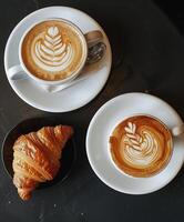 zwei Tassen von Kaffee und ein Croissant auf ein Tabelle foto