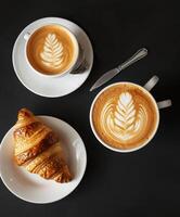 zwei Tassen von Kaffee und ein Croissant auf ein Tabelle foto