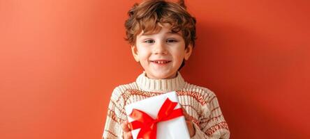 glücklich jung Junge halten ein Geschenk mit ein rot Bogen auf ein Orange Hintergrund. lächelnd Kind im ein gemütlich Pullover. Konzept von Freude, Feier, Überraschung, Urlaub Geist foto
