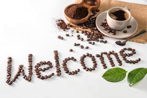 Kaffeetasse und Text aus Kaffeebohnen, isoliert auf weiss. Text das Wort Willkommen aus Kaffeebohnen. Schriftart