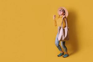 Porträt eines aufgeregten schönen Mädchens mit Kleid und Sonnenbrille mit Einkaufstüten. fröhliche junge Frau mit Handtasche auf gelbem Hintergrund. Shopaholic Shopping-Mode. foto