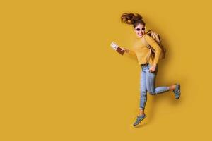 Reisender mit Koffer, Reisepass mit Ticket auf gelbem Hintergrund. Porträt des lächelnden glücklichen Mädchens im gelben Kleid. Menschen Reisender foto