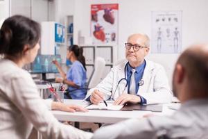 Oberarzt mit grauen Haaren bei Patientenuntersuchung foto