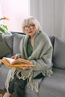 altmodische ältere Frau, die auf der Couch sitzt und zu Hause ein Buch liest. Bildung, Reife, Freizeitkonzept foto