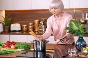 Senior fröhliche Frau kocht in der modernen Küche. Essen, Fähigkeiten, Lifestyle-Konzept