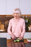 Senior fröhliche Frau kocht in der modernen Küche mit dem Laptop. Essen, Bildung, Lifestyle-Konzept