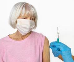 verängstigte ältere Frau in Maske und Arzthände in medizinischen Handschuhen mit Spritze während der Impfung auf weißem Hintergrund. Gesundheitsversorgung, Impfkonzept