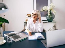 müde senior schöne graue Haare Frau in weißer Bluse am Laptop im Büro arbeiten. Arbeit, Senioren, Probleme, Lösung finden, Konzept erleben foto