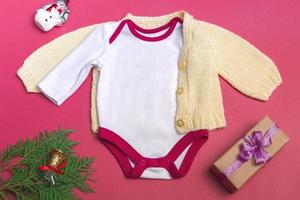 Weihnachten weißes Baby Body Mockup auf farbigem Hintergrund Nahaufnahme - mit gestrickter gelber Jacke - Mockup von Neugeborenenkleidung. Platz kopieren foto
