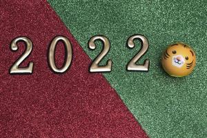 Neujahrskonzept goldene Zahlen 2022 mit Tigergesicht auf grün-rotem Glitzerhintergrund mit Kopierraum foto