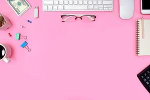Draufsicht oder flacher rosa Pastellschreibtisch mit Computer, Bürobedarf und Kaffeetasse