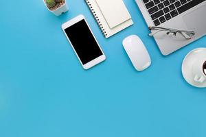 Draufsicht blauer pastellfarbener Schreibtisch mit Computer, Büromaterial, Handy und schwarzer Kaffeetasse foto