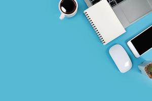 Arbeitsplatztisch mit Laptop, Bürobedarf, Kaffeetasse, Handy und Kaffeetasse auf blauem Pastellhintergrund foto