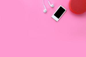 Pause am technologieorientierten Geschäftstisch mit Musikplayer, Ohrhörer und drahtlosem tragbarem Lautsprecher auf rosafarbenem Pastellhintergrund