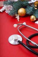 medizinisches Stethoskop und Weihnachtsschmuck auf rotem Grund. Weihnachtsmedizinisches Konzept