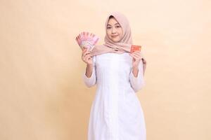 asiatisch Muslim Frau im Hijab lächelt halten Rupiah Kasse und Anerkennung Karte im Hand. Lebensstil, religiös, Geschäft und Finanzen Konzepte foto