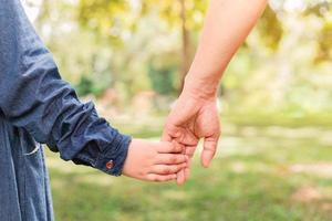 Kind, das die Hand des Vaters hält, geht im Park spazieren foto