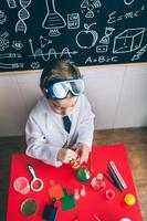Kind spielt mit chemischen Flüssigkeiten über Tisch foto