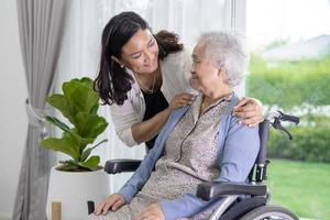 Die Tochter der Pflegekraft hilft einer asiatischen Seniorin oder einer älteren alten Dame, die im Rollstuhl sitzt und eine Gesichtsmaske trägt, um die Sicherheitsinfektion des Covid-19-Coronavirus zu schützen. foto