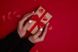 Valentinstag Zusammensetzung. Hand hält Geschenkbox mit Schleife und roten Herzen Konfetti.