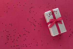 Weihnachtskomposition. Geschenkbox mit rotem Band und Konfetti-Dekorationen auf buntem Hintergrund aus Pastellpapier. Weihnachten, Winter, Neujahrsfeierkonzept. flach legen, Ansicht von oben, Platz kopieren foto
